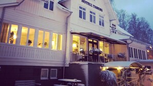 A two-story building with a sign reading "HOTEL TABERG." It features large windows, a balcony, and a snow-covered ground.