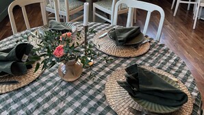 A dining area with checkered tablecloths, white chairs, and woven placemats.