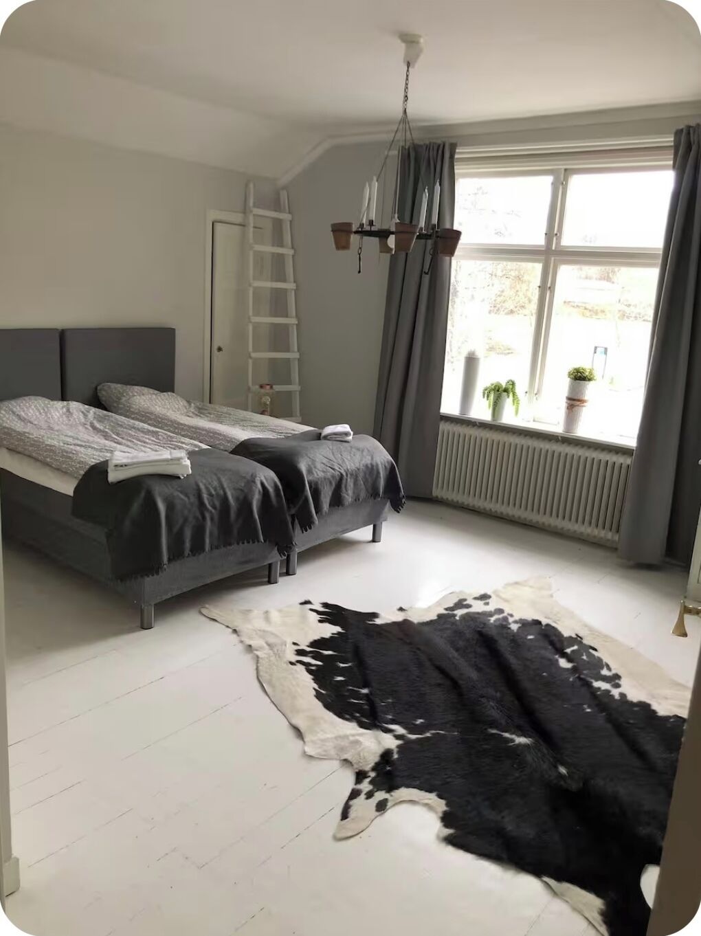 Ein Schlafzimmer mit zwei Betten, einer Himmelsleiter, einem großen Fenster mit Vorhängen und einem Kuhfellteppich.