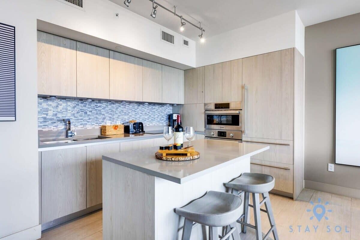 A modern kitchen with a central island, bar stools, and a tiled backsplash.