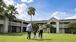 A family walking on a grassy lawn in front of a building with multiple balconies and palm trees. - Orlando Vacation Rooms (Kissimmee)