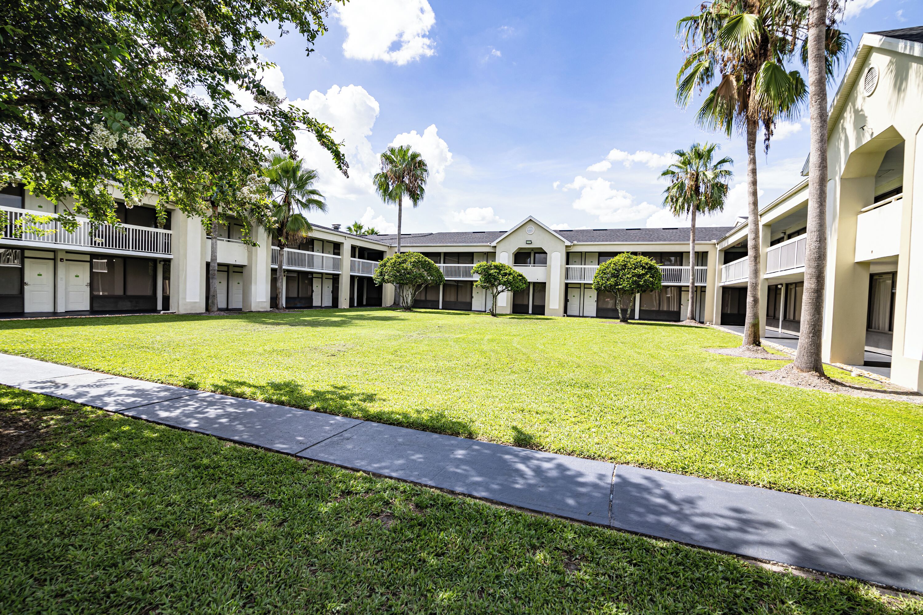 A courtyard with a lawn, palm trees, and a building with multiple balconies.