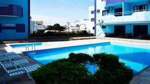 Zona de piscina con sillas de descanso y un edificio con fachada de azulejos.