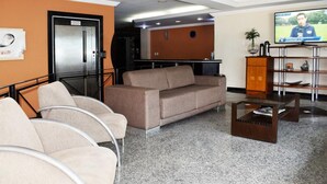 Un hall con un sofá, sillas, una mesa de centro, un televisor y un mostrador de recepción.