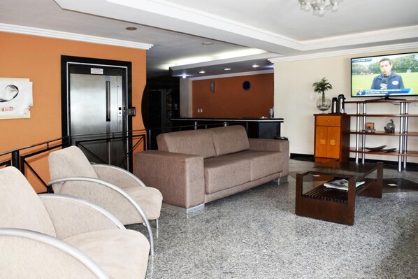 A lobby with a sofa, chairs, a coffee table, a TV, and a reception desk. - Norte Palace Hotel (Sao Mateus)