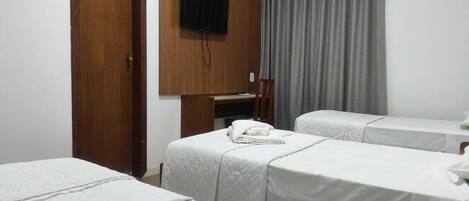 Habitación de hotel con dos camas individuales, un armario de madera, un televisor montado en la pared y una cortina gris.
