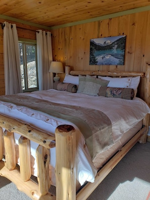 Une chambre à coucher dans une cabane en bois, avec un lit, des oreillers, un tableau et une fenêtre avec des rideaux.