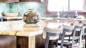 Une cuisine avec un îlot central en bois, un vase en verre et des chaises en osier.