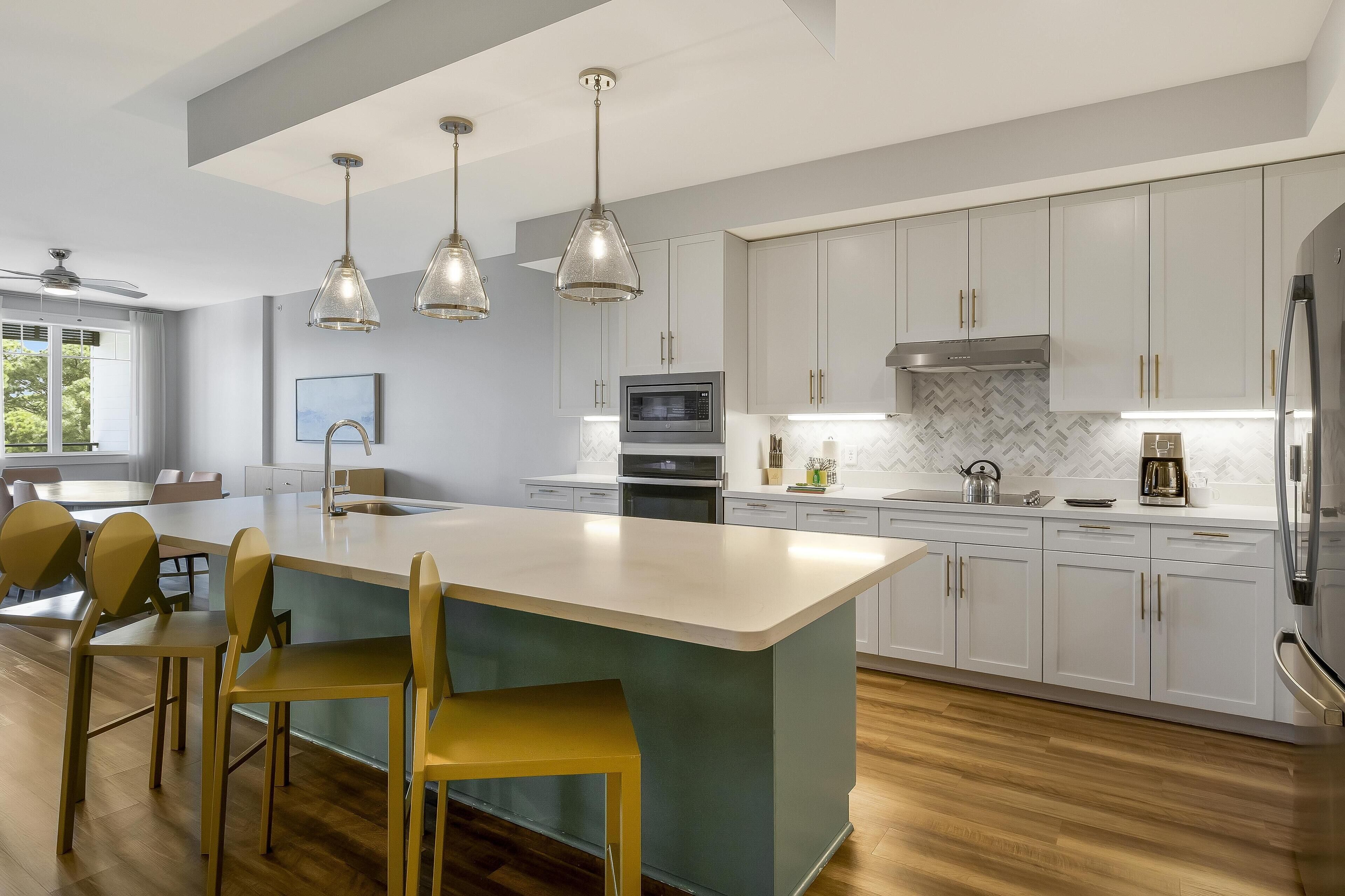 A modern kitchen with a central island, pendant lighting, and a herringbone-patterned backsplash.