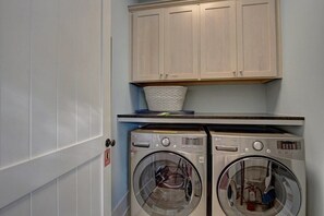 A laundry room with two front-loading washing machines, a cabinet above, and a basket on the countertop. - A Little Overboard, Private Pool/Spa, Easy walk to Beach, Golf Cart Included! (WaterSound)