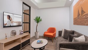 A modern living room with a flat-screen TV, a potted plant, an orange armchair, a grey sofa, and a coffee table. - Citadines Amigo Iloilo (Iloilo)