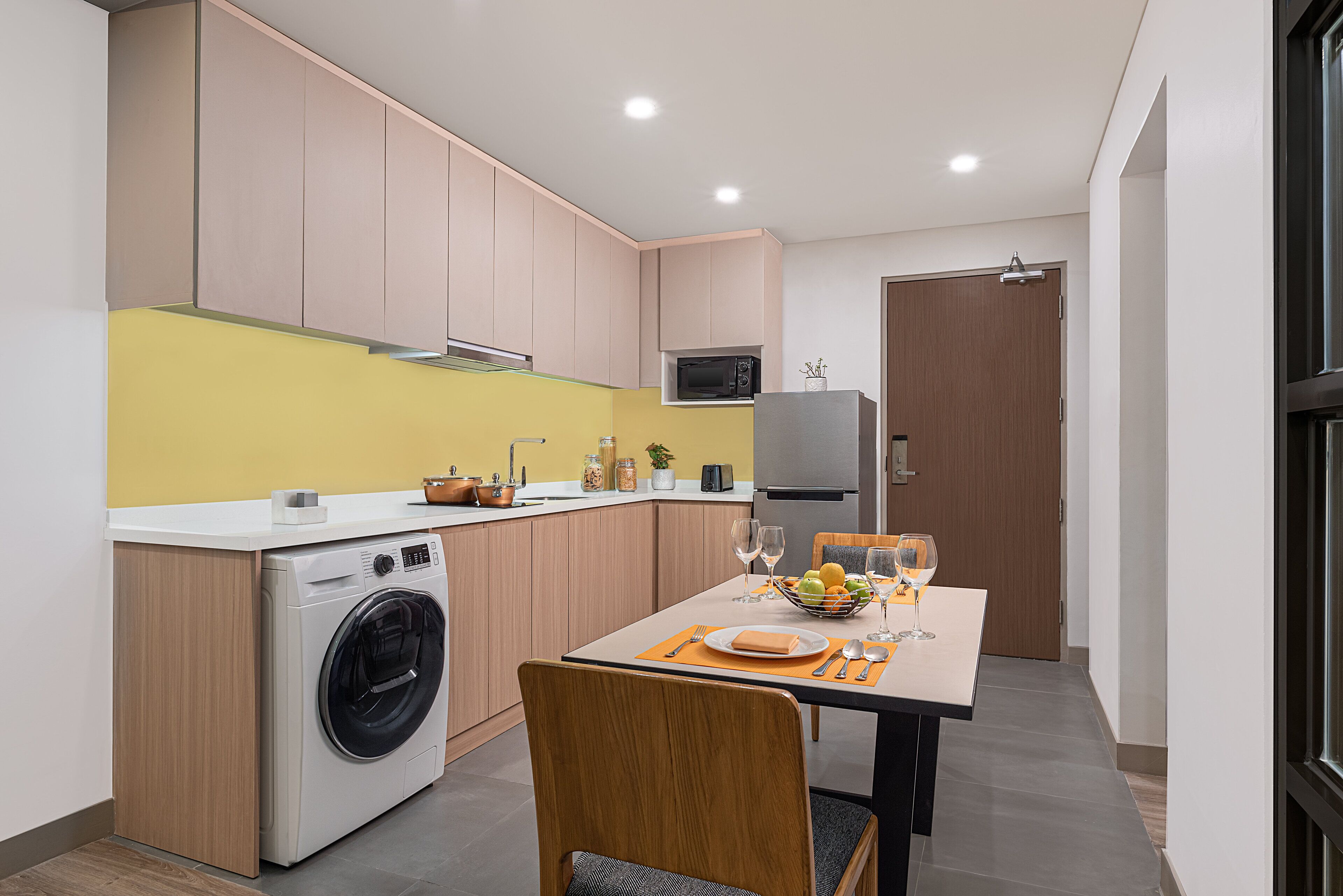 Cocina compacta con lavadora, microondas y comedor con mesa para dos.