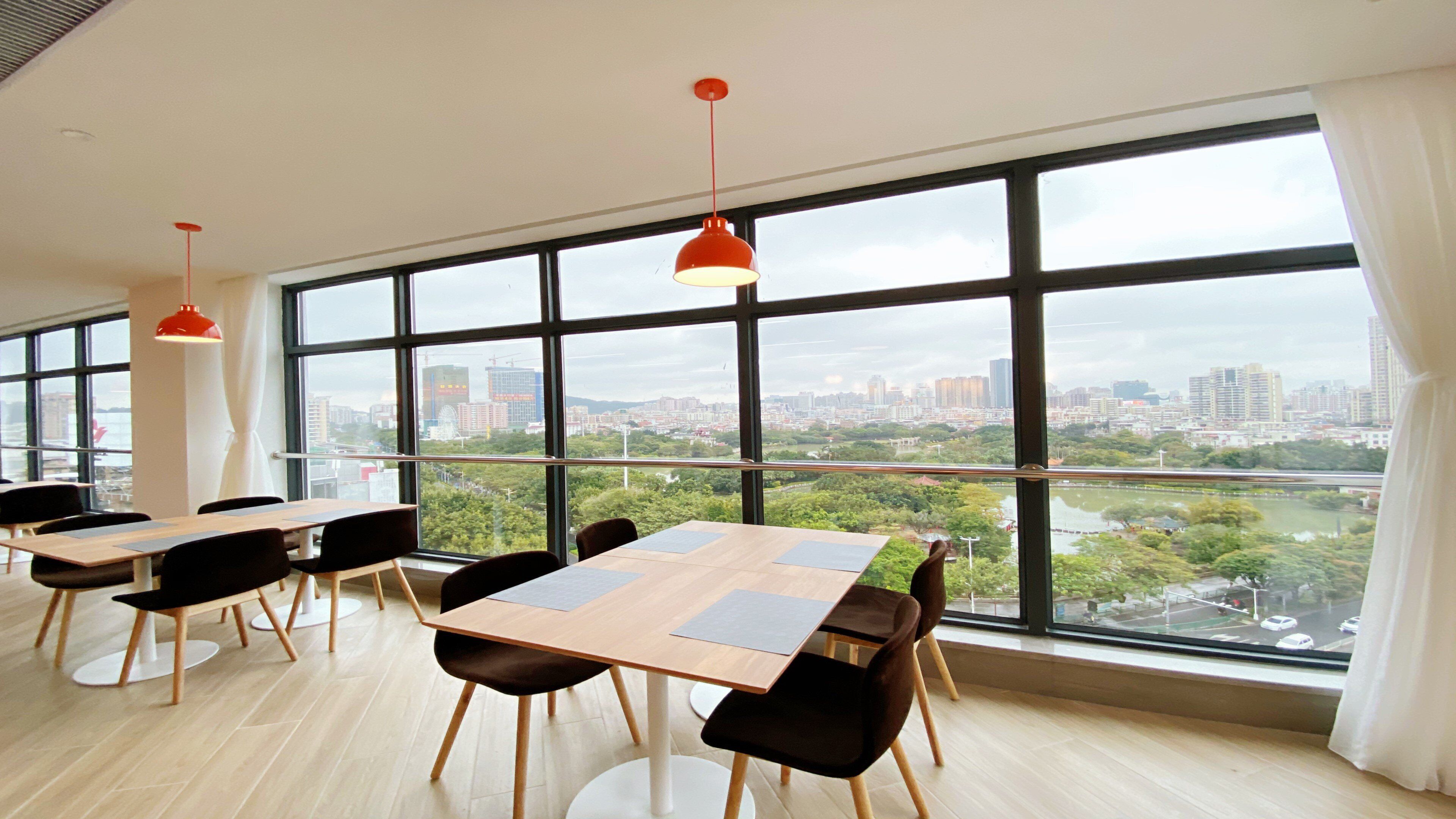 Une salle de conférence moderne, dotée de grandes fenêtres, de tables en bois et de chaises noires.