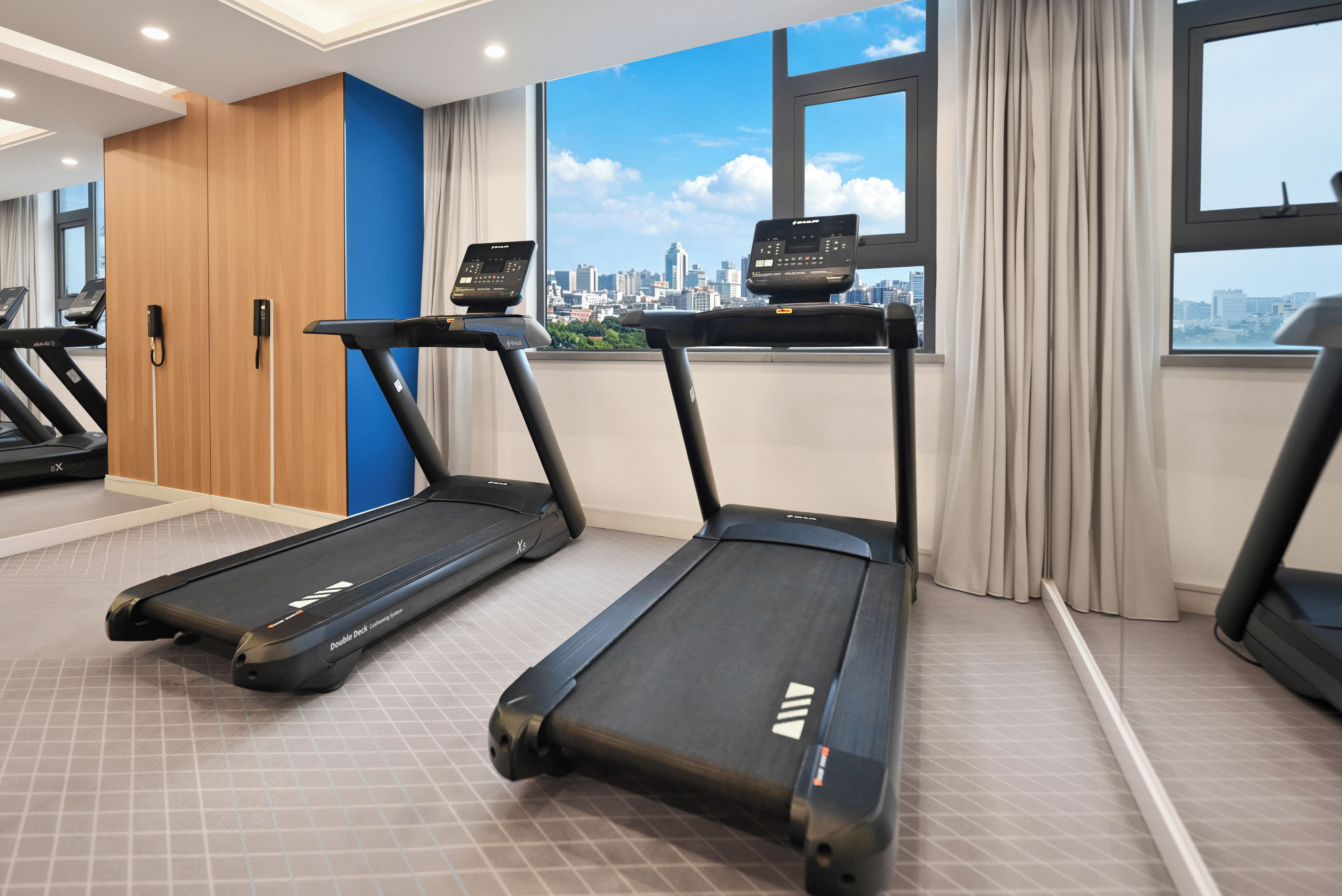 A gym with treadmills, a cityscape view, and a blue accent wall.