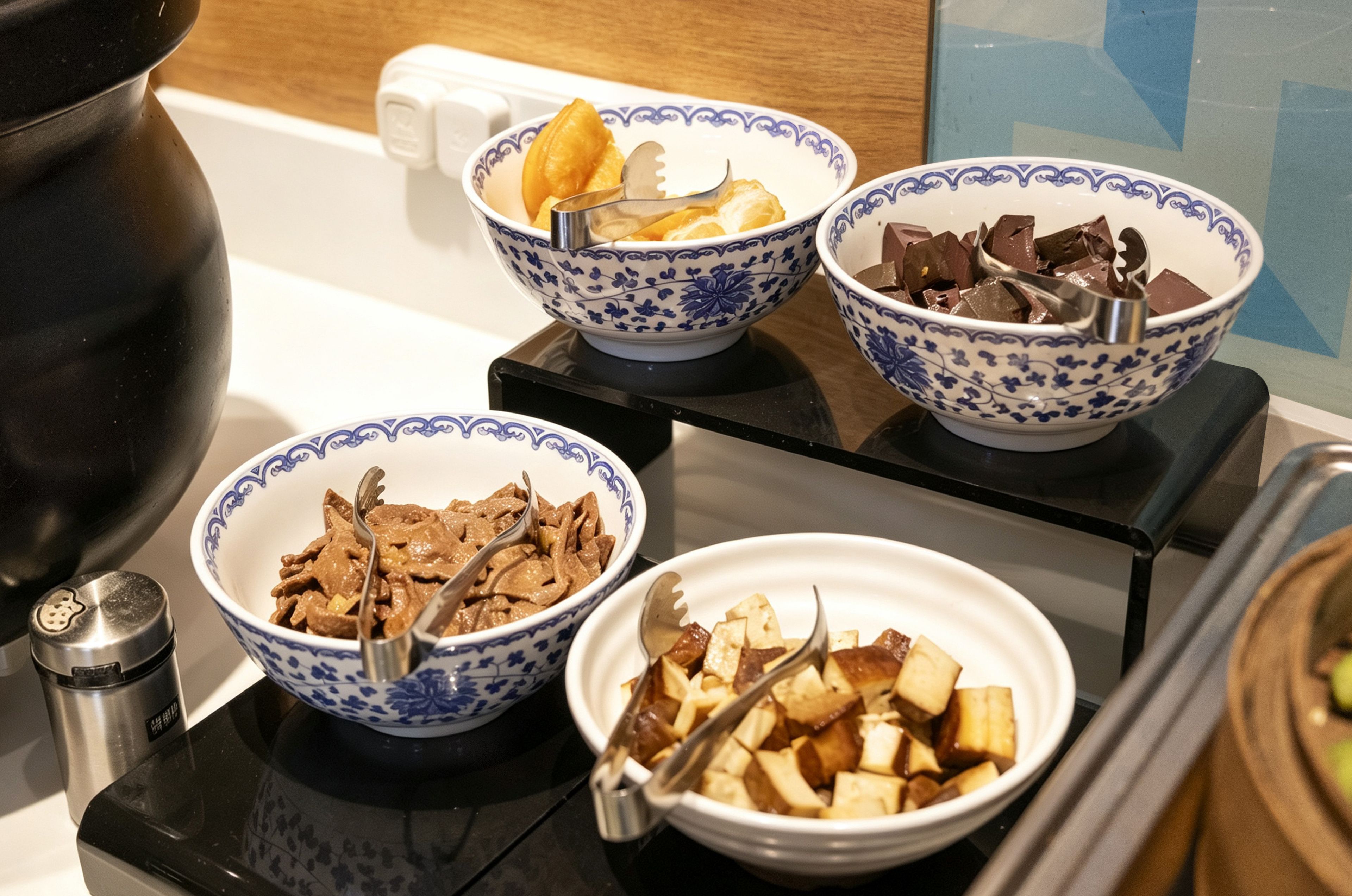 A kitchen counter with three bowls containing food items, a salt shaker, and a kettle.