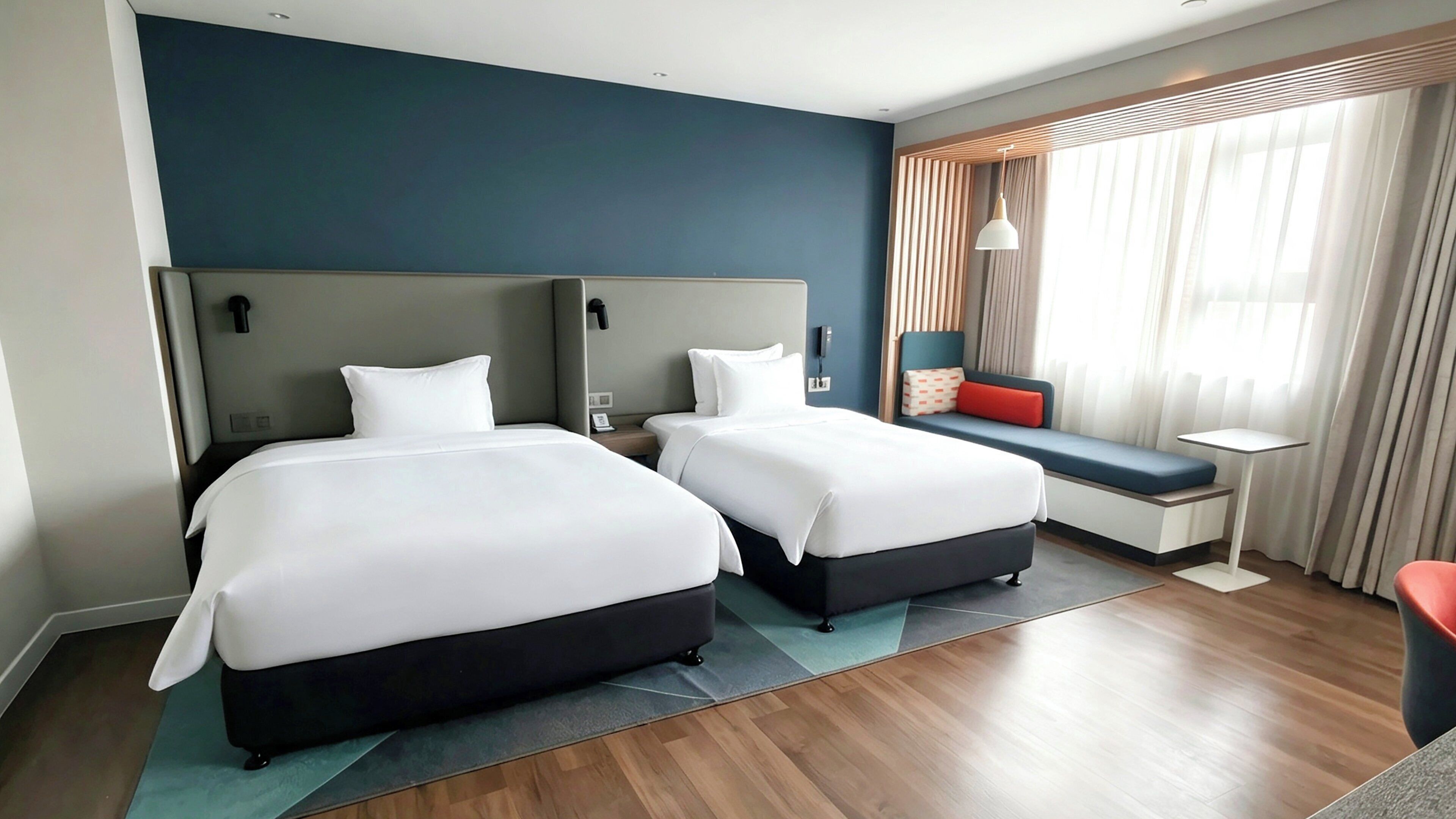 A hotel room with two beds, a seating area, a small table, and a window with curtains.