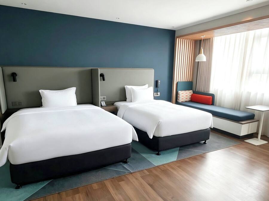 A hotel room with two beds, a seating area, a small table, and a window with curtains.