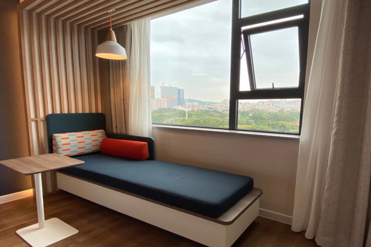 A single bed with a view of a cityscape through a window.