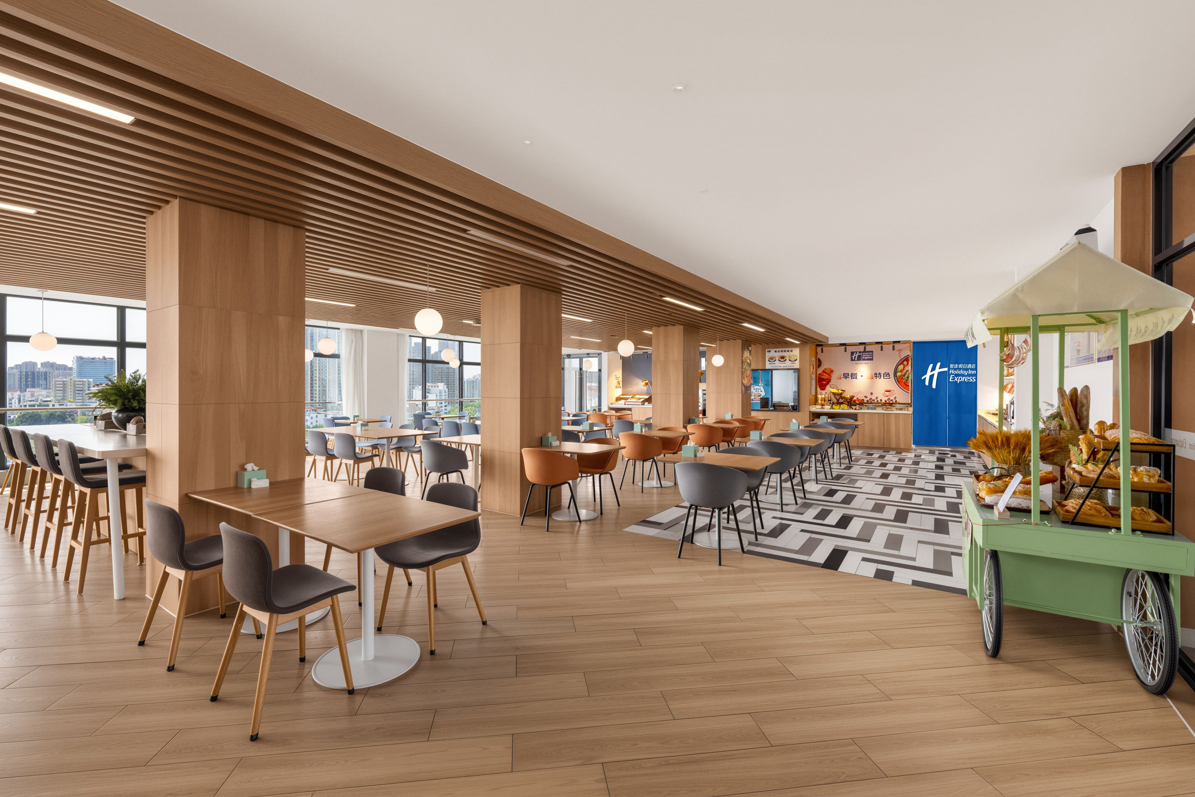 A modern hotel lobby with wooden flooring, multiple seating areas, and a food cart.