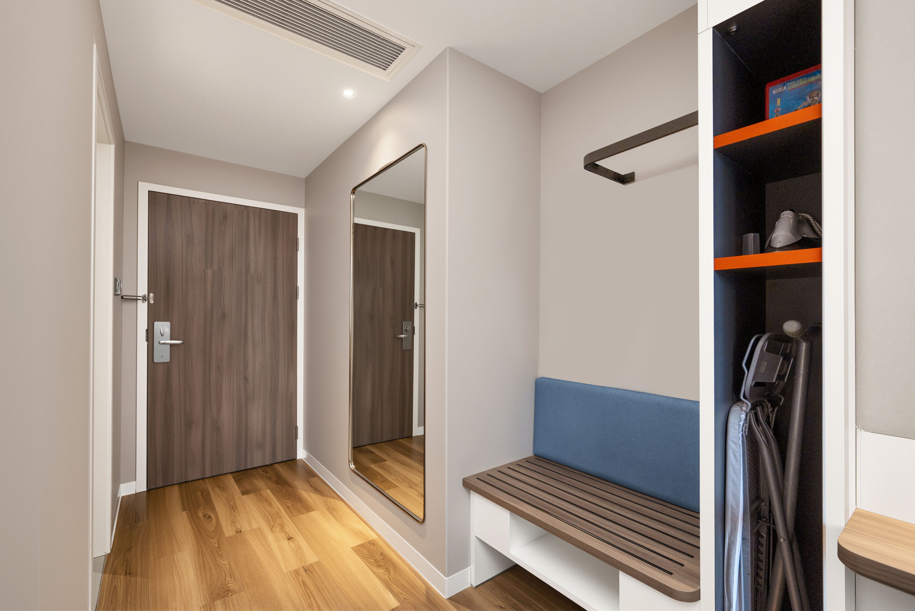 A modern hallway with a wooden door, a bench, a mirror, and a shelving unit with a towel rack.