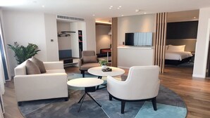 Une chambre d’hôtel moderne dotée d’un espace salon comprenant un canapé, deux fauteuils, une table basse et un téléviseur.