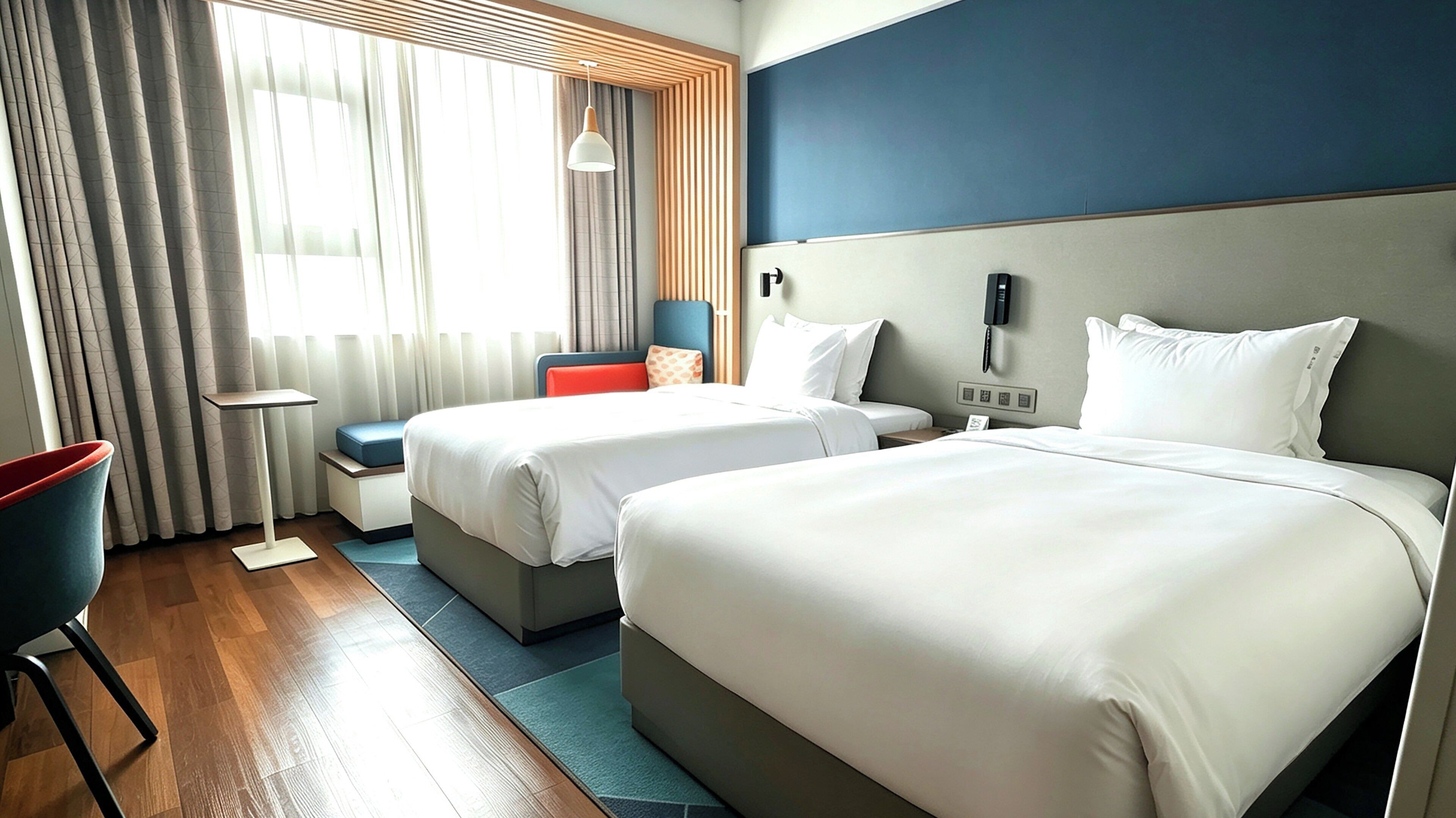 Hotellihuone, jossa on kaksi sänkyä, työpöytä, tuoli ja seinälle asennettu puhelin.