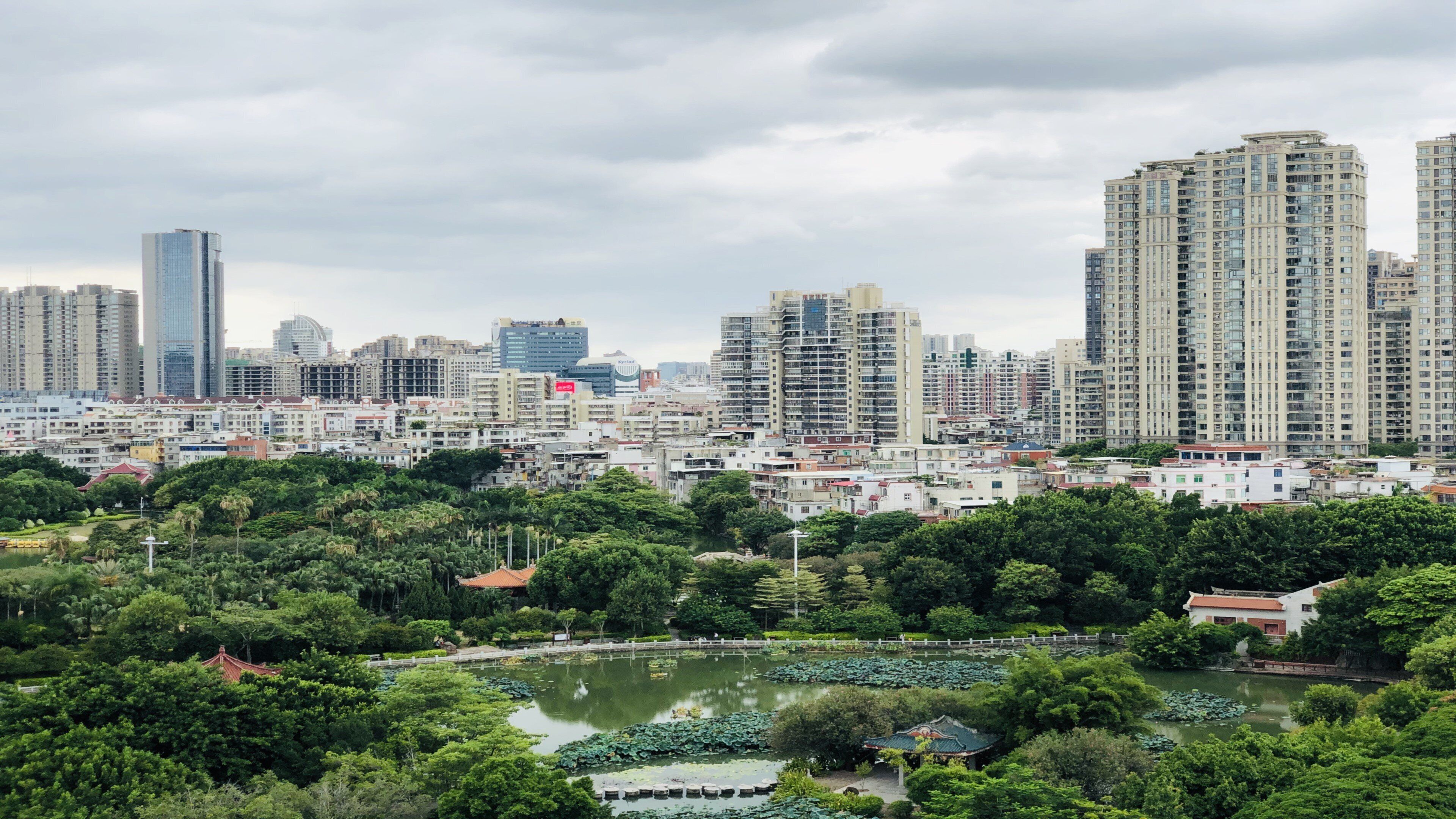 A cityscape with high-rise buildings and a park with a pond.