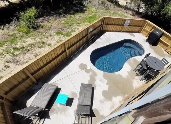 A backyard with a swimming pool, a wooden deck, and outdoor furniture.
