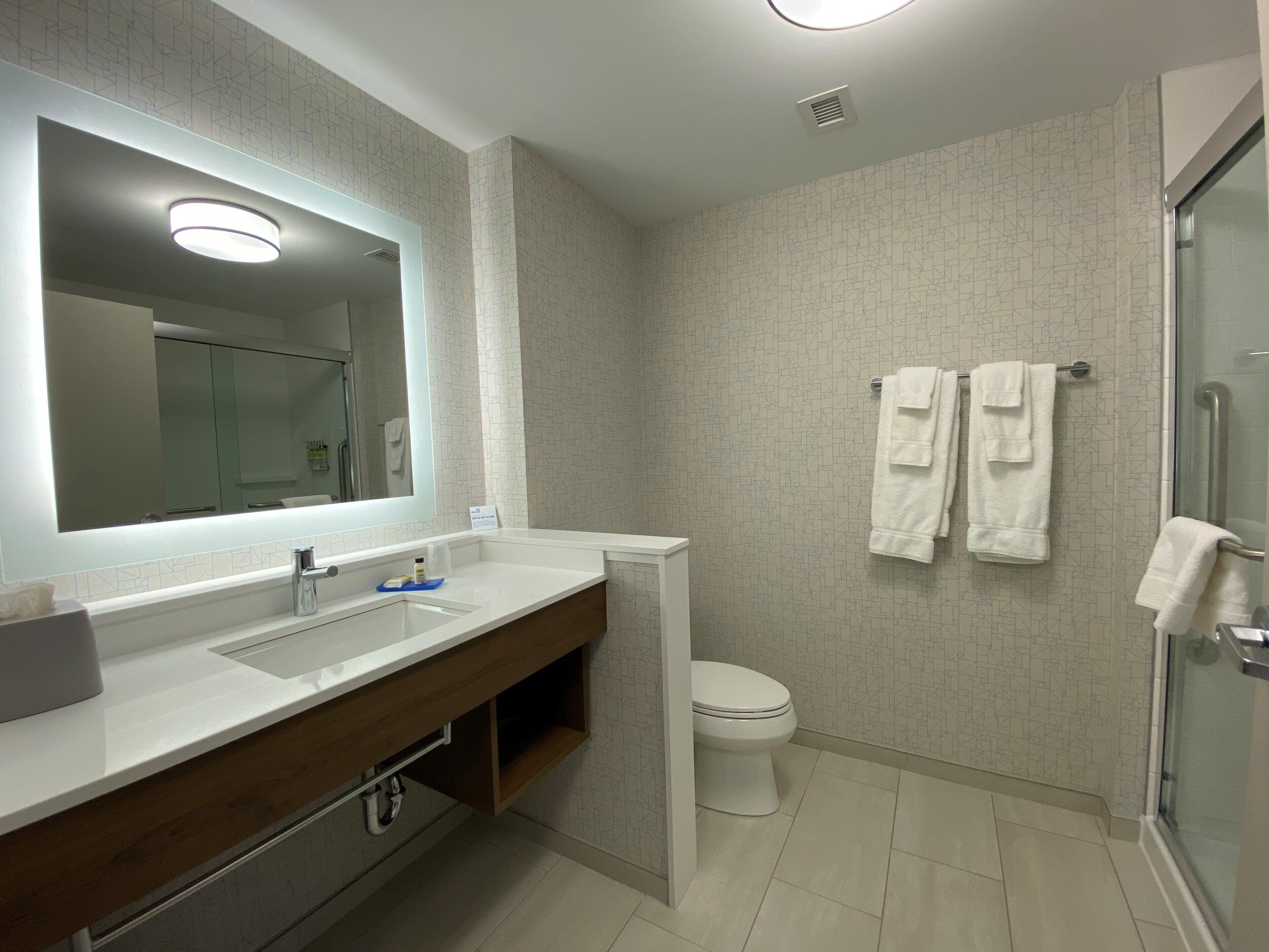 A modern bathroom with a large mirror, a sink, a toilet, and a shower area.