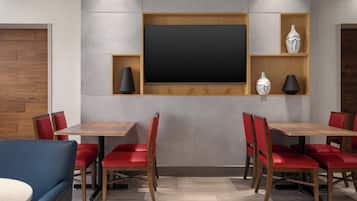 A modern dining area with a large flat-screen TV, wooden tables, red chairs, and decorative vases.