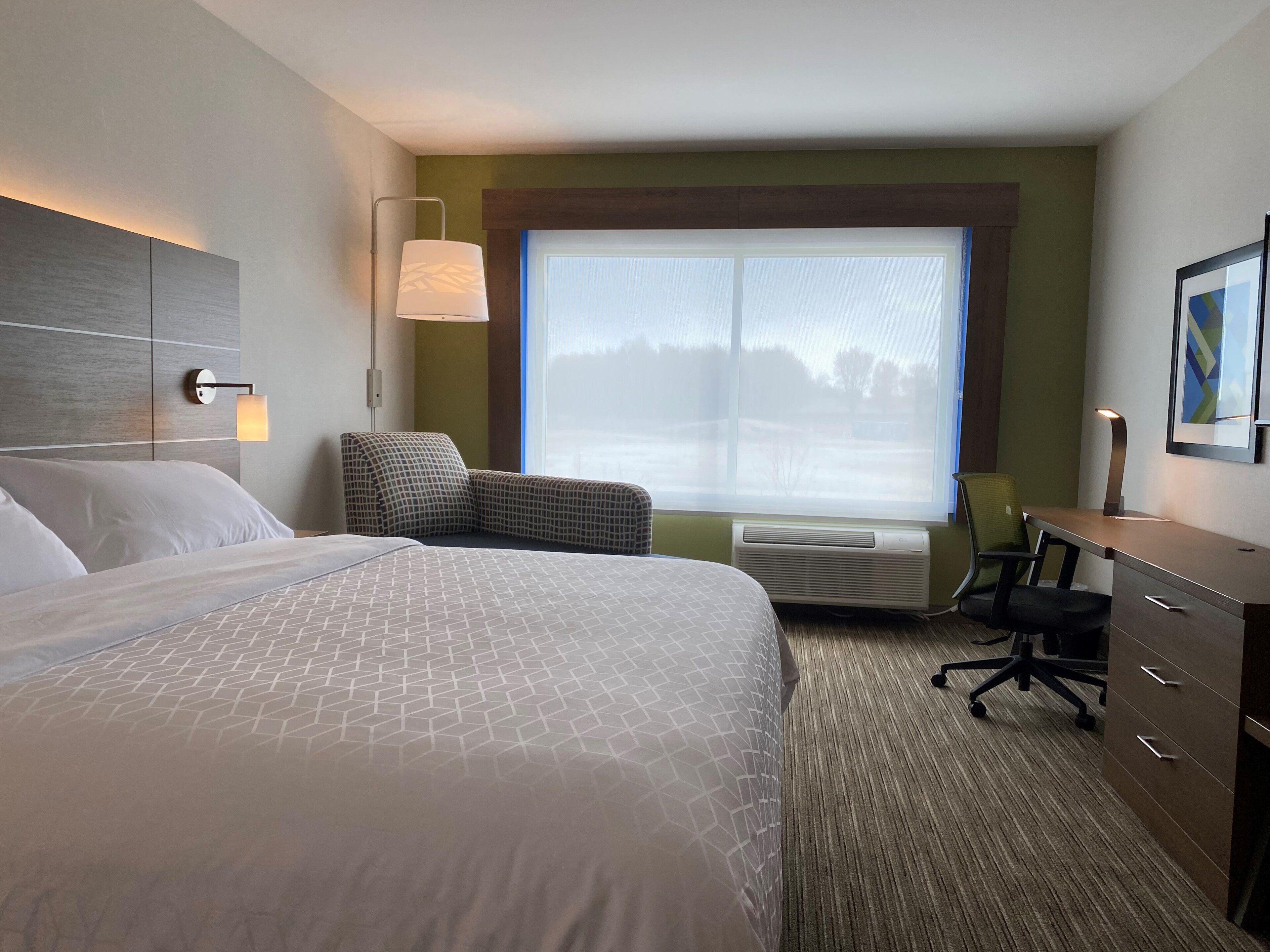 Habitación de hotel con una cama grande, un escritorio, una silla, una ventana con vistas y aire acondicionado.