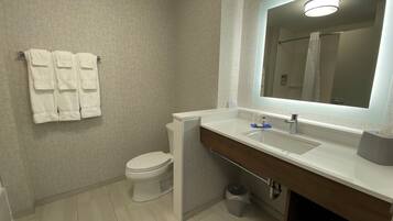 Un baño moderno con un lavamanos, espejo y retrete blancos. Toallas blancas cuelgan de la pared.