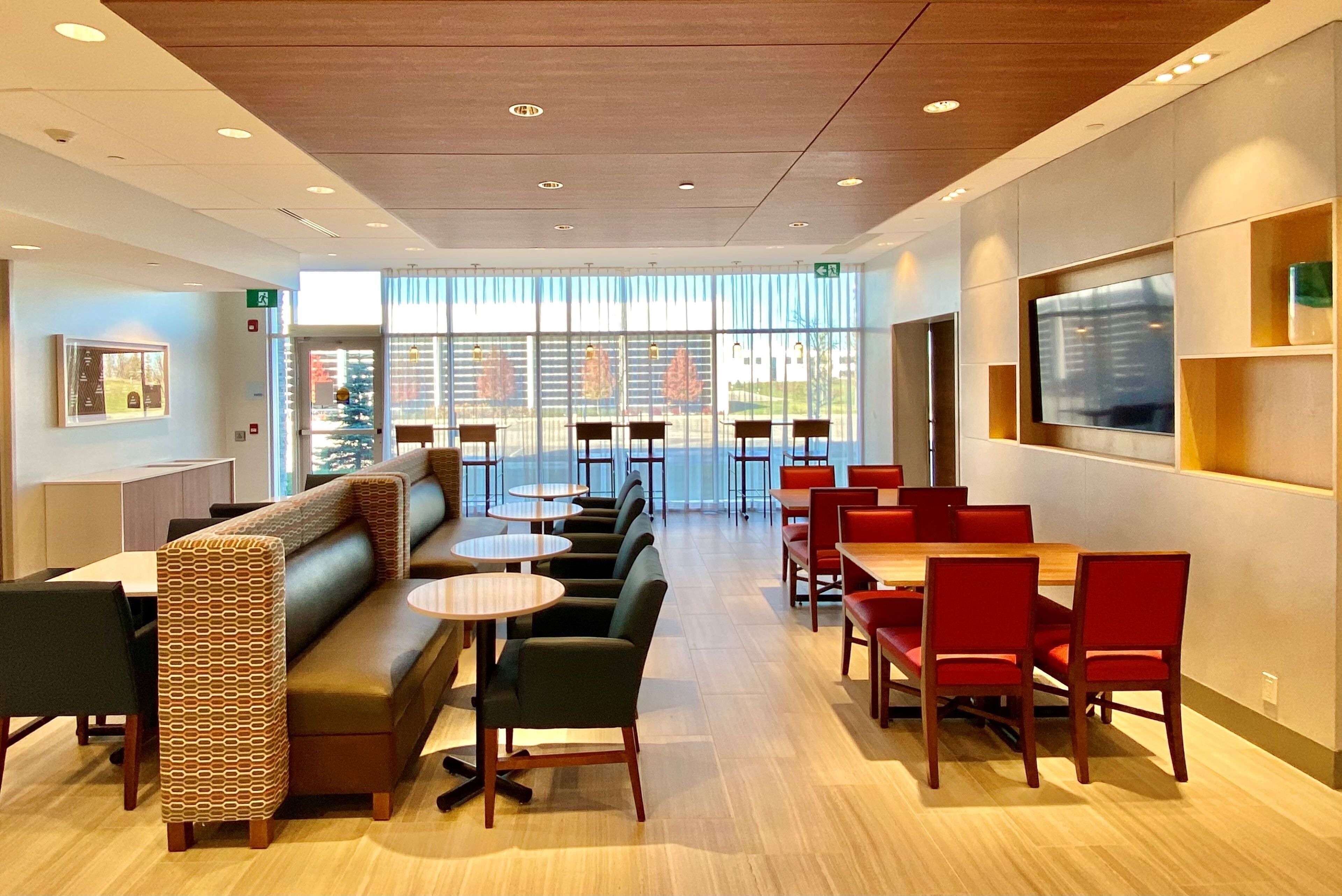 A modern hotel lobby with a seating area, tables, and a large window offering a view.