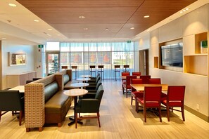 A modern hotel lobby with a seating area, tables, and a large window offering a view. - Holiday Inn Express & Suites Aurora by IHG (Aurora)