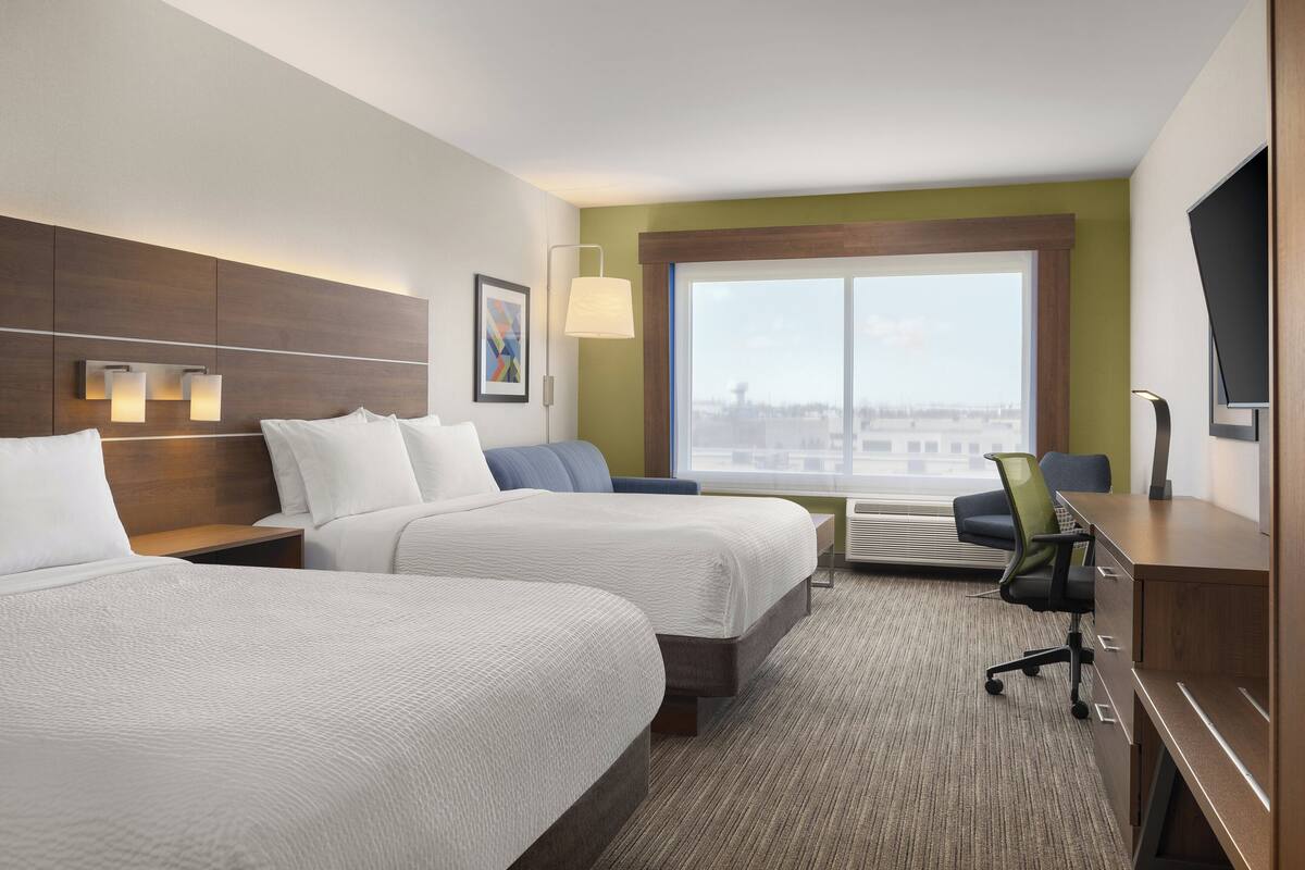 Une chambre d’hôtel avec deux lits, un bureau, une chaise, une télévision, une fenêtre donnant sur la ville et un tableau au mur.