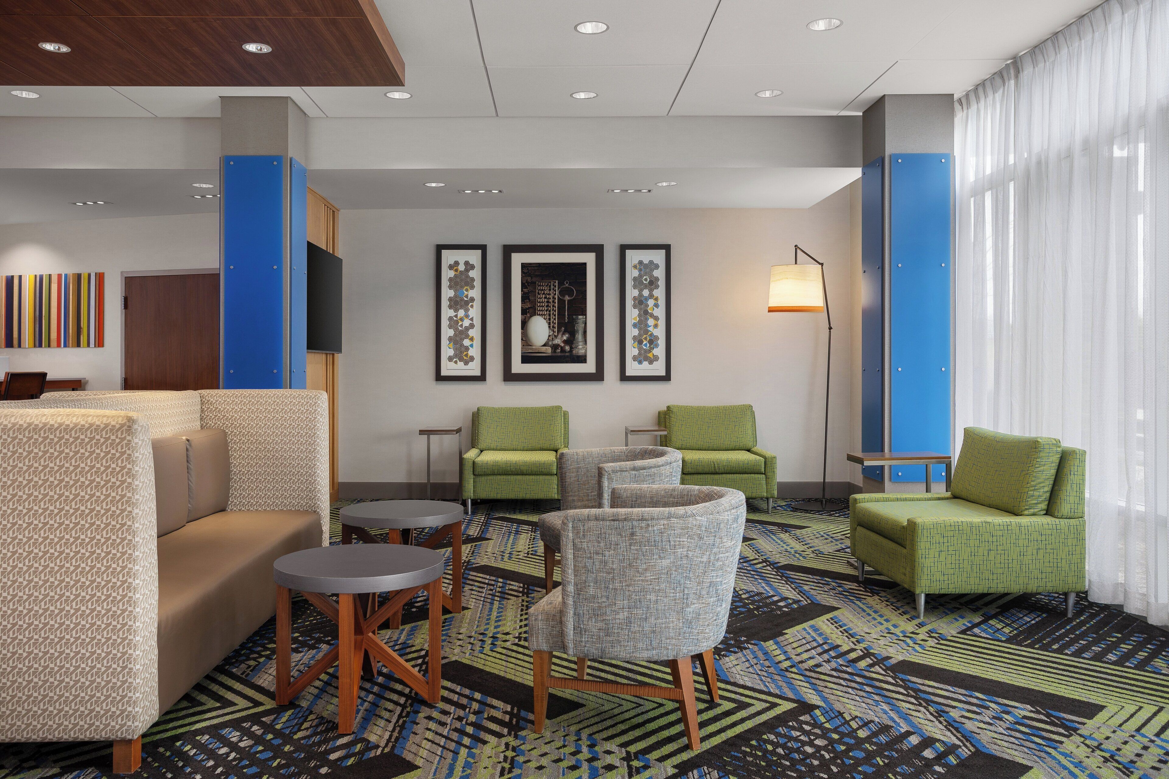A hotel lobby with a sofa, chairs, a small table, framed artwork, and a lamp.