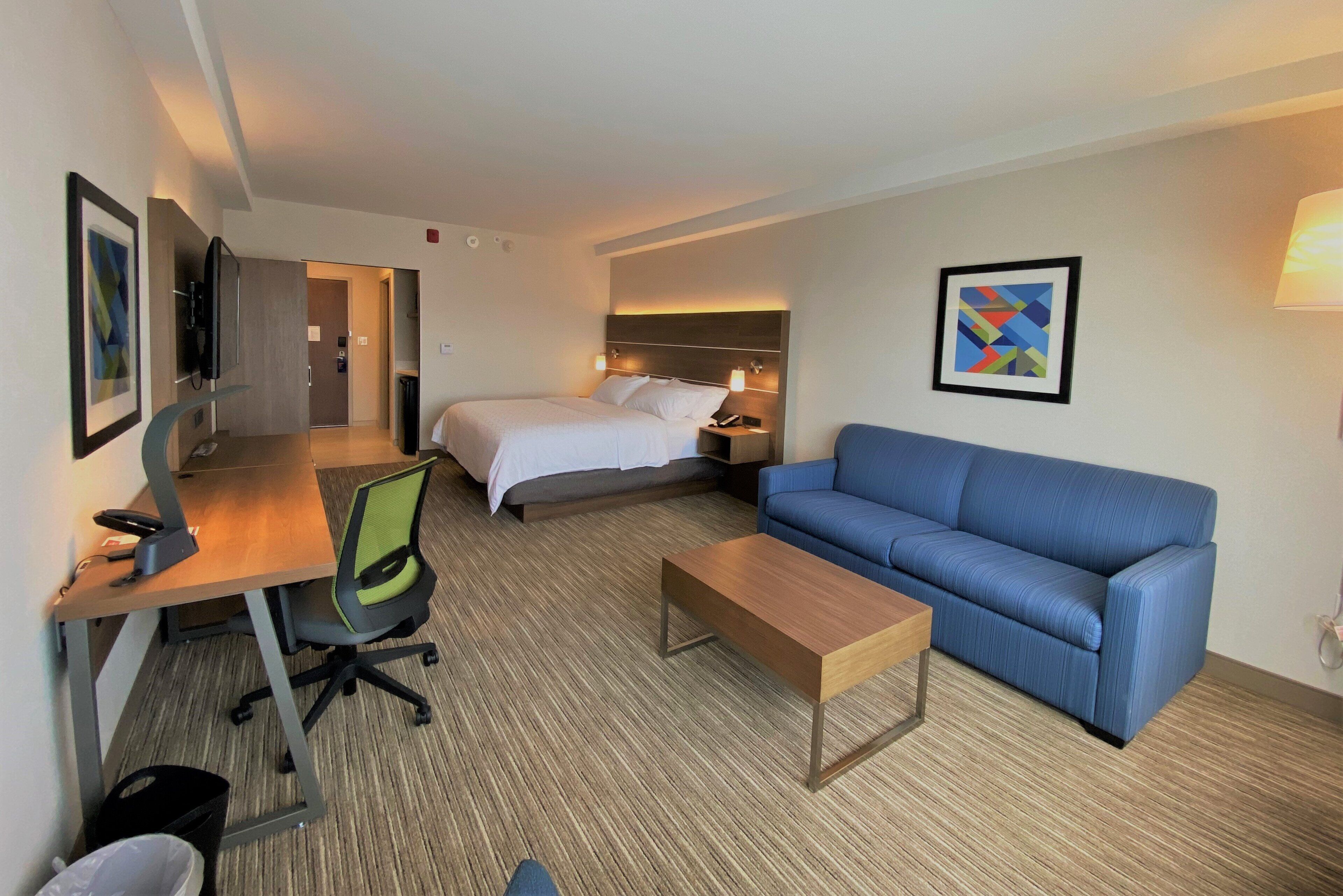 Une chambre d’hôtel avec un lit, un canapé bleu, un bureau avec une chaise, une petite table et un téléviseur.