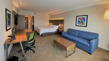 Une chambre d’hôtel avec un lit, un canapé bleu, un bureau avec une chaise, une petite table et un téléviseur.