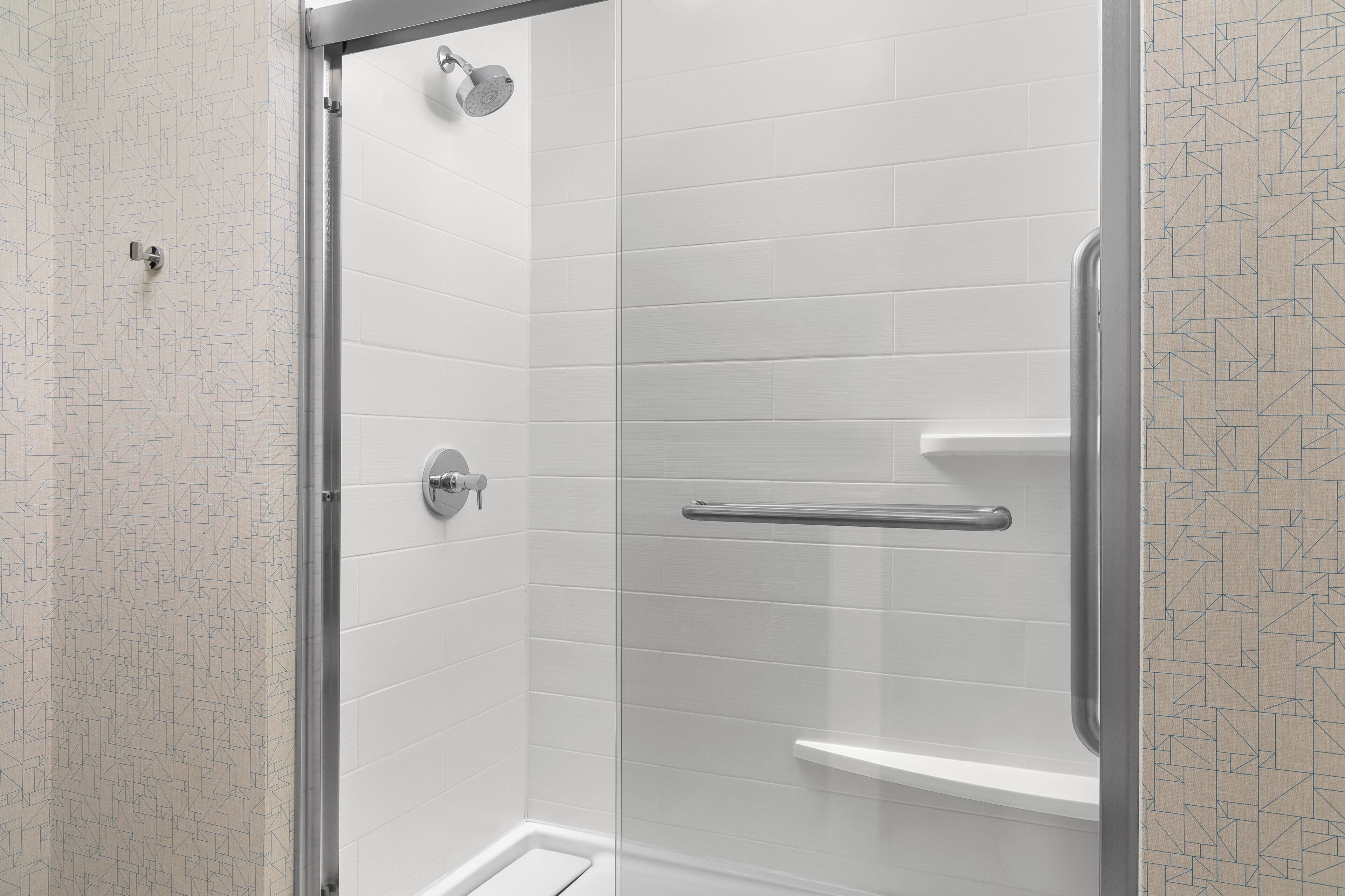 A shower with a glass door, a handrail, and a showerhead.