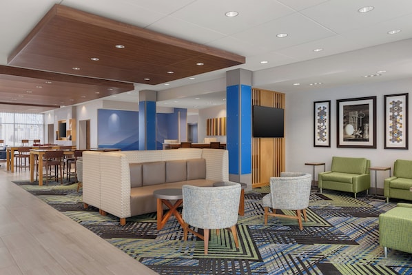 A modern hotel lobby with a seating area, a reception desk, and framed artwork on the walls. - Holiday Inn Express & Suites Aurora by IHG (Aurora)