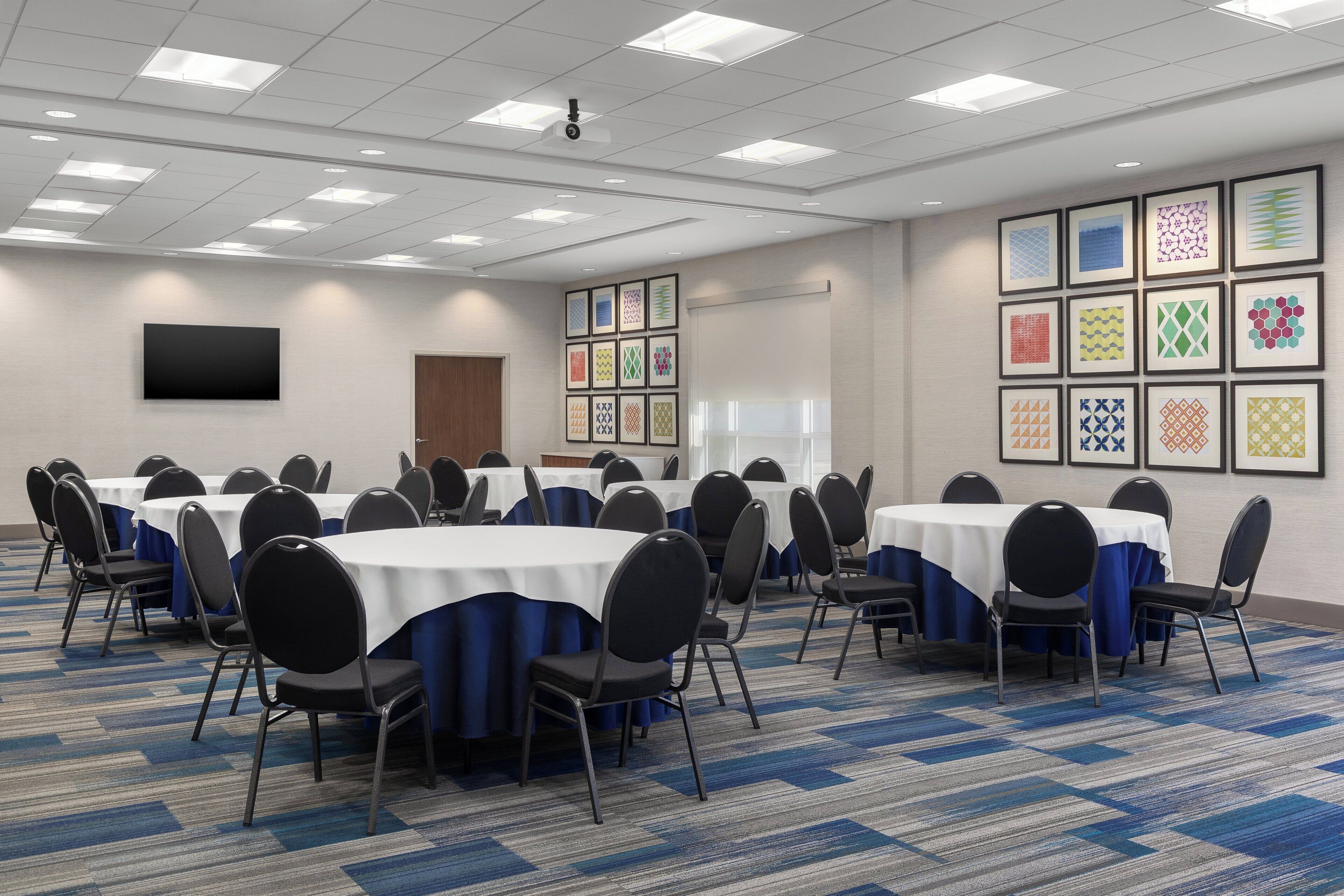 A conference room with tables, chairs, a projector, and framed patterns on the walls.