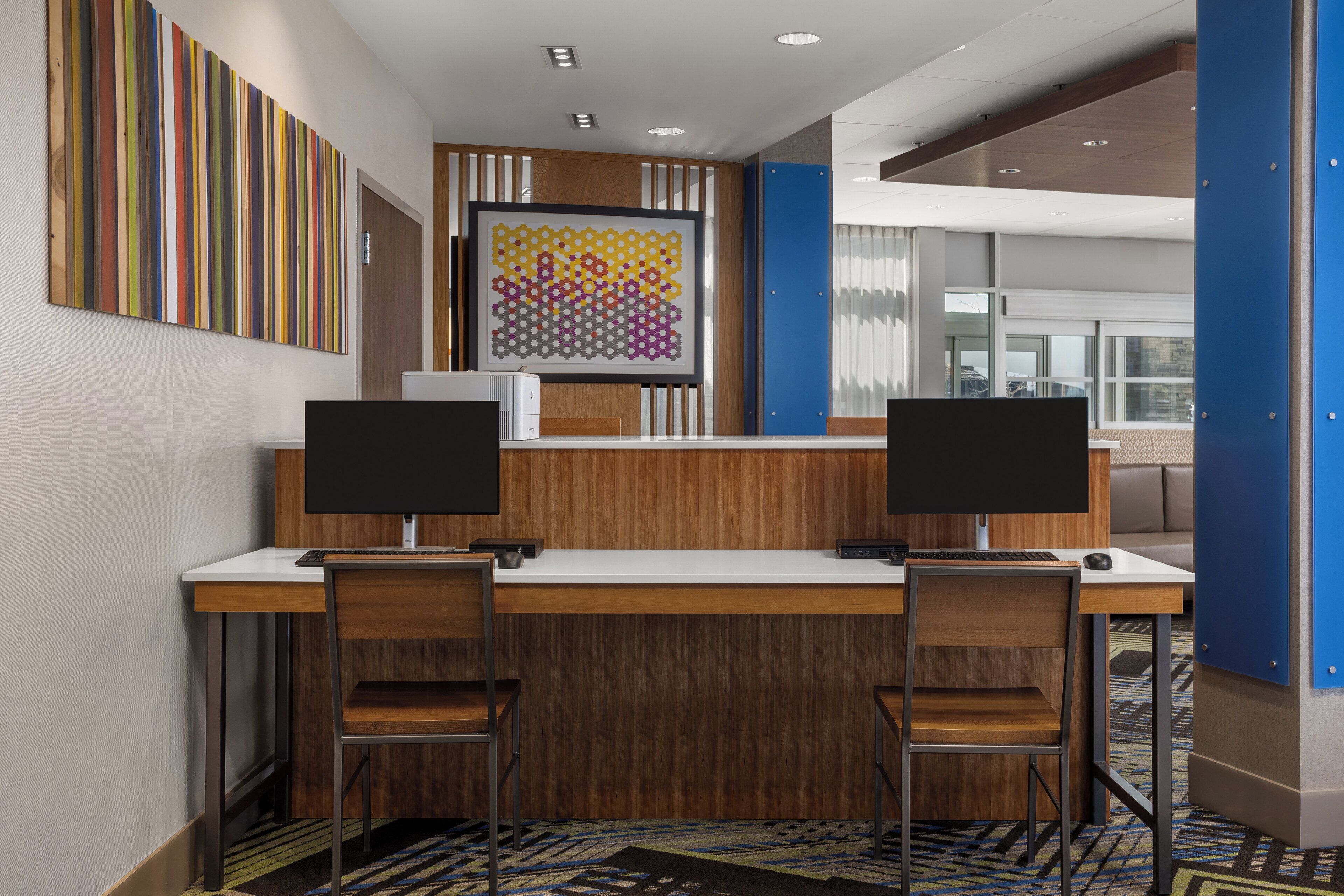 A reception desk with two computer monitors, wooden paneling, and a patterned artwork on the wall.