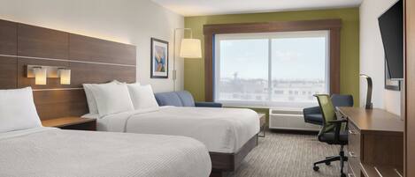 A hotel room with two beds, a desk, a chair, a TV, a window with a city view, and a painting on the wall.