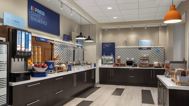 A modern breakfast area with a self-serve station, a bakery section, and a counter with various food items. - Holiday Inn Express & Suites Aurora by IHG (Aurora)