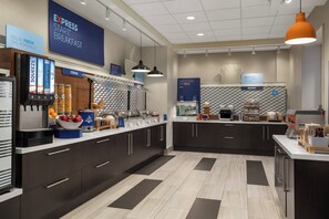 A modern breakfast area with a self-serve station, a bakery section, and a counter with various food items. - Holiday Inn Express & Suites Aurora by IHG (Aurora)