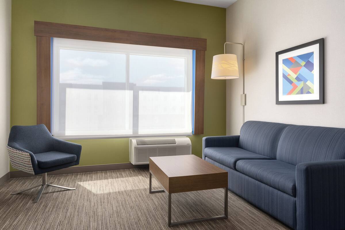 Une pièce avec une grande fenêtre, un canapé, un fauteuil, une table et une lampe fixée au mur.