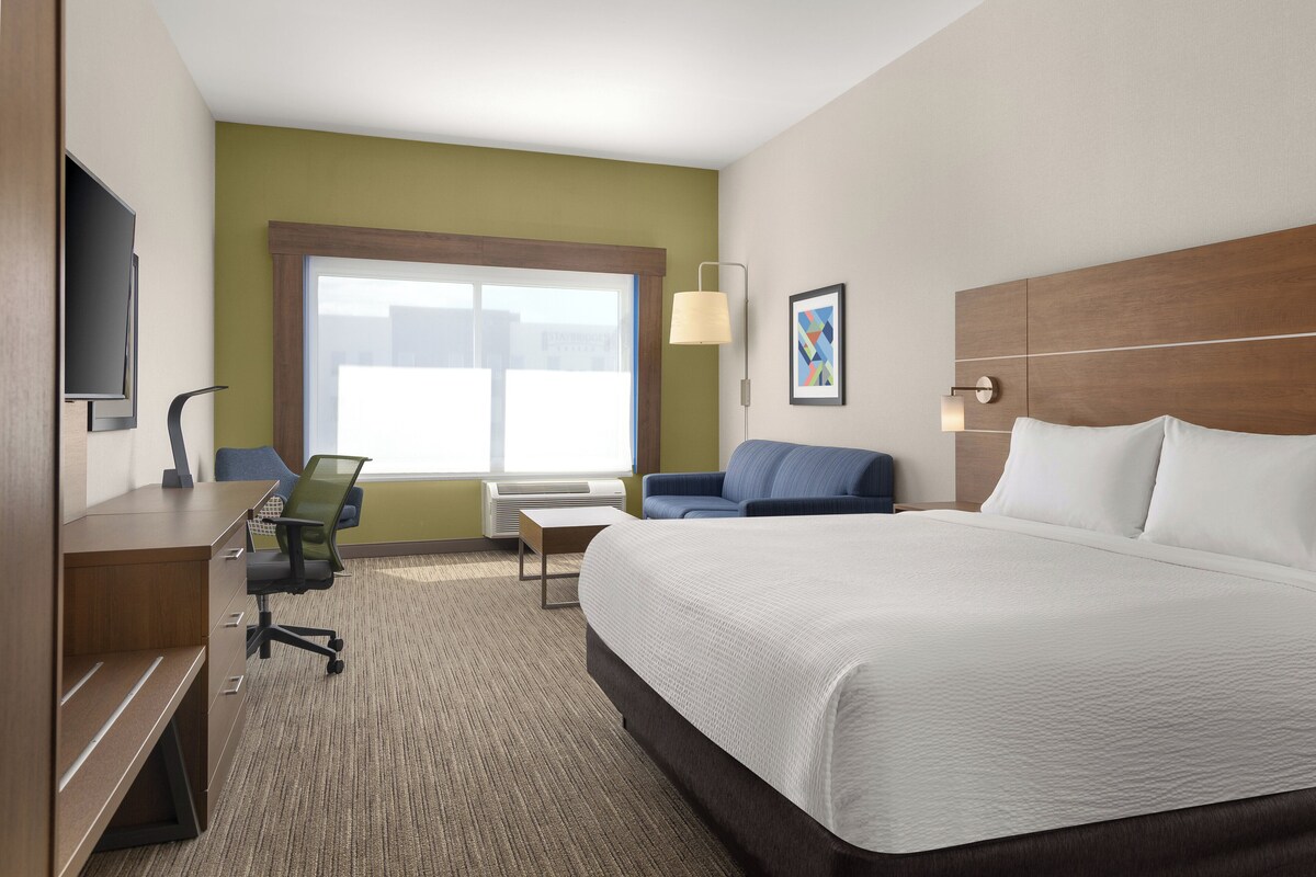 A hotel room with a bed, desk, chair, and a large window.