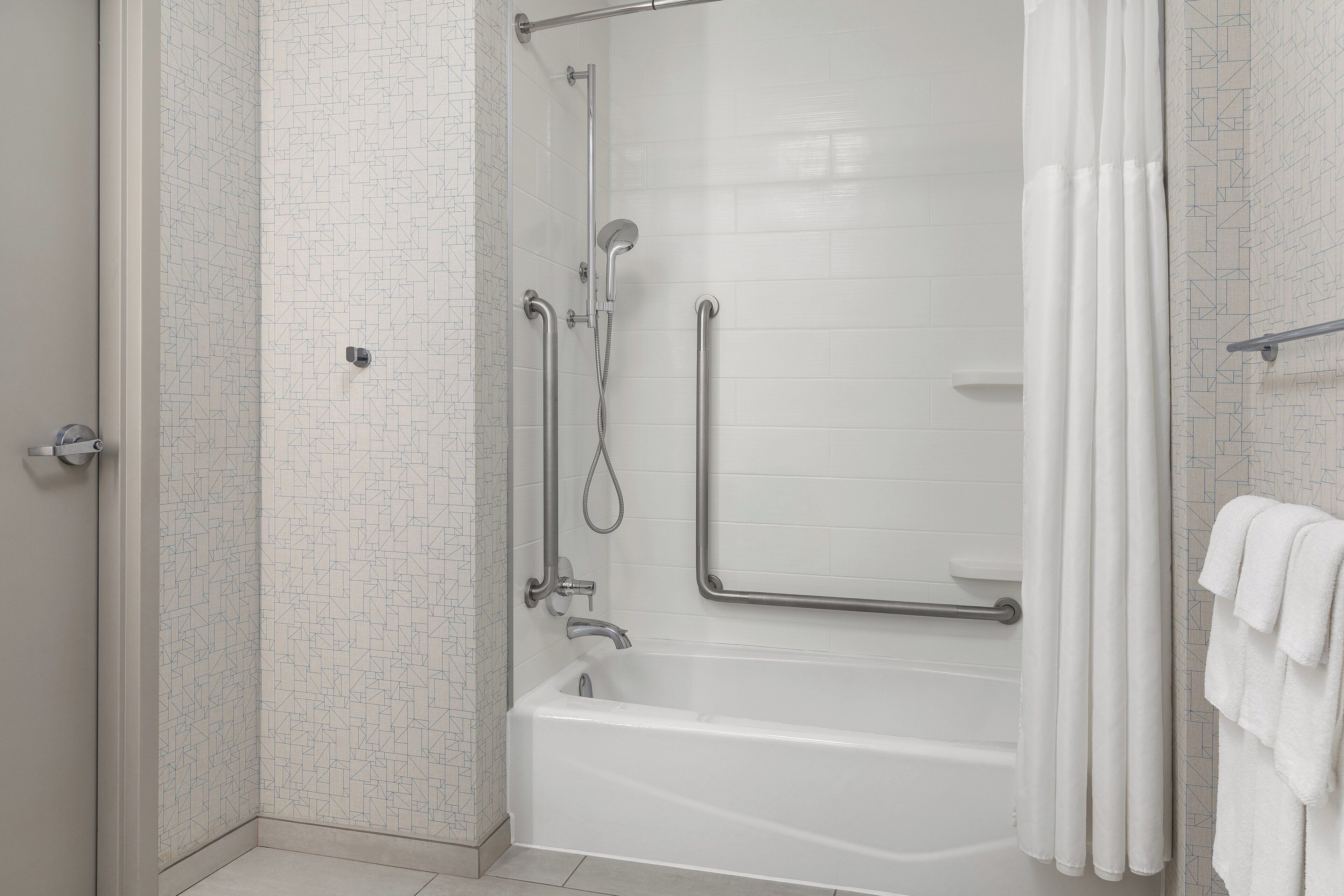 A modern bathroom with a walk-in shower, grab bars, and a bathtub.