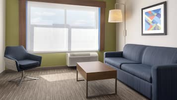 A room with a large window, a sofa, a chair, a table, and a wall-mounted lamp.
