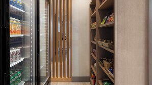 A narrow hallway with a refrigerator stocked with beverages, a wooden divider, and shelves with snacks and toiletries. - Holiday Inn Express & Suites Aurora by IHG (Aurora)